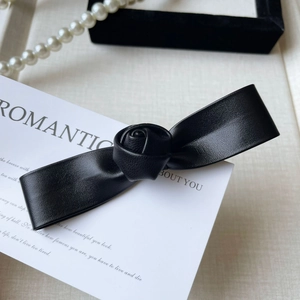 Détail de la pince à cheveux noeud en cuir noir avec rose centrale sur carte