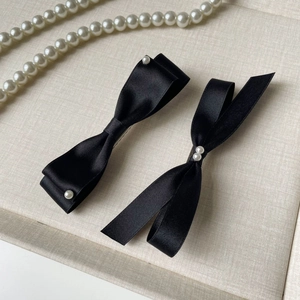 Elegant black fabric bow hair clips with pearls on a textured cream tray