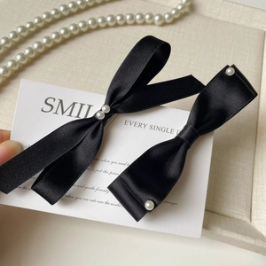 Detailed macro view of black satin bow hair clips with elegant white pearl accents