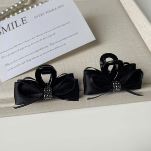 Pair of black ribbon bow hair claws with sparkling rhinestones on fabric background