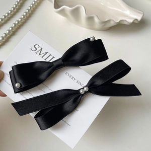 Detail of elegant black satin bow hair clips featuring delicate pearl embellishments