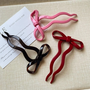 Three bow-shaped hair forks in pink, black, and burgundy with a glossy finish