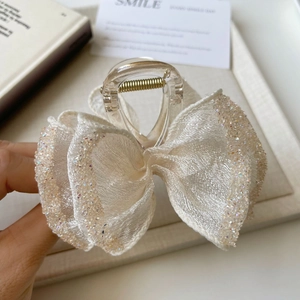 Close-up of a large cream bow hair claw clip with shimmering rhinestones and gold spring
