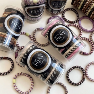 Set of multi-colored woven elastic hair ties in a clear cylindrical storage container