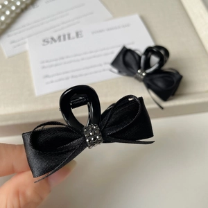Detailed close-up of a black satin ribbon bow hair claw clip with shimmering grey rhinestones