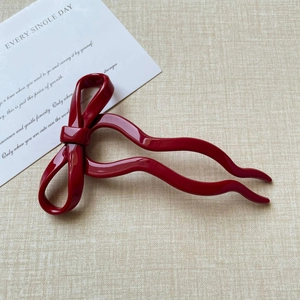Close-up of a glossy red bow hair pin with a wavy design on a textured beige fabric