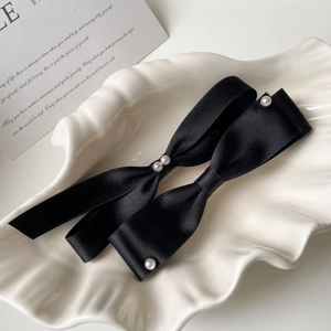 Detail of elegant black silk bow hair clips with white pearls on a ceramic shell tray