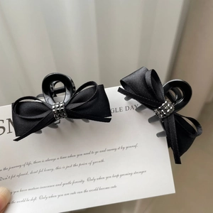 Close-up of two black silk bow hair clips with dark rhinestones on a display card