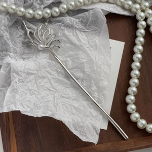 Detailed close-up of a silver butterfly hair pin with pearls and zircon on a wooden tray