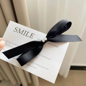 Detail of a black fabric bow hair clip with twin white pearls on a white display card