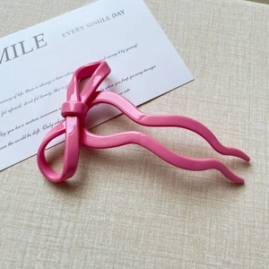 Detail shot of a pink ribbon bow hair pin made of smooth glossy resin on fabric background
