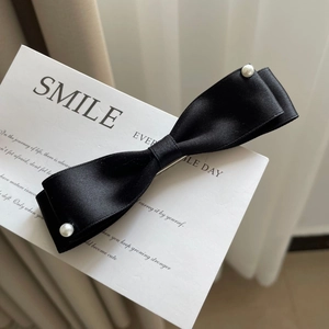 Detail view of a black silk bow hair clip with elegant white pearls on a white card
