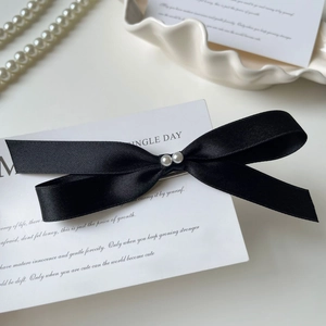 Detailed close-up of a black satin bow hair clip with pearls on a white porcelain plate