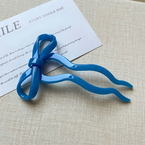 Macro detail of sky blue ribbon hair pin with glossy finish on a white decorative card