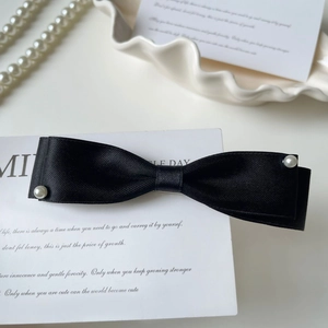 Detail of elegant black satin bow hair clip with pearls on a white display tray