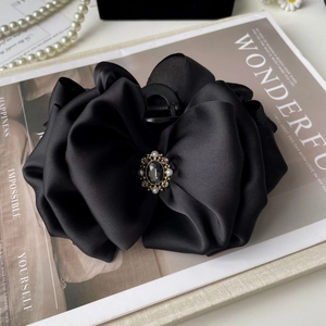 Detail of black satin bow hair claw clip with vintage jewel on a fashion magazine
