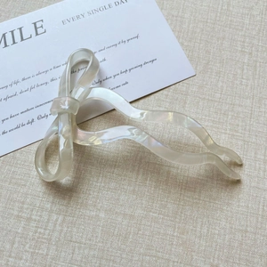 Close-up of pearlescent bow hair fork with wavy design on beige textured fabric
