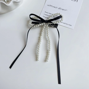 Detalle de pasador de lazo con cinta negra y borlas de perlas en cascada elegantes