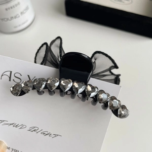 Détail d'une pince à cheveux noire avec nœud en tulle et strass brillants en cœur