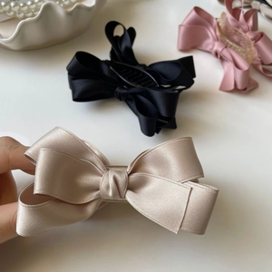 Dettaglio di eleganti fermagli per capelli a fiocco in raso beige, nero e rosa su sfondo