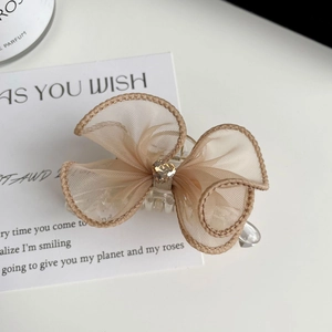 Détail de pince à cheveux nœud en maille beige avec cristal en cœur sur carte blanche