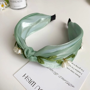 Detail eines hellgrünen Satin-Haarreifs mit Knoten und zarten Maiglöckchen-Blüten-Applikationen
