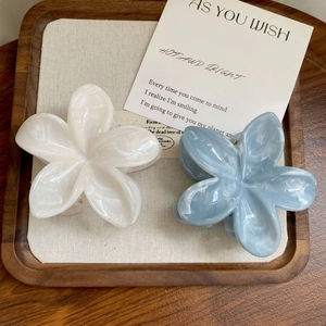 Detail of cream white and misty blue marble acetate flower hair claws on a wood tray