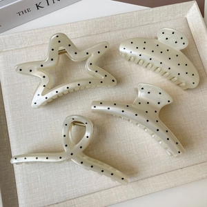 Close-up of four creamy white hair claws with black polka dots and gold springs