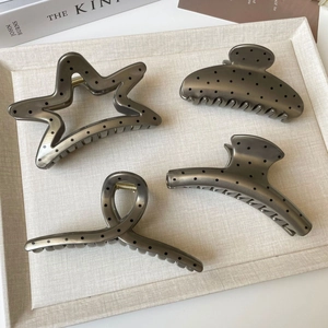 Detail of four grey metal hair claws with black polka dots in various shapes on a tray