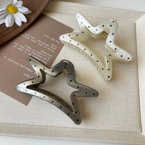 Close-up of star-shaped hair claws with polka dot patterns in creamy white and taupe
