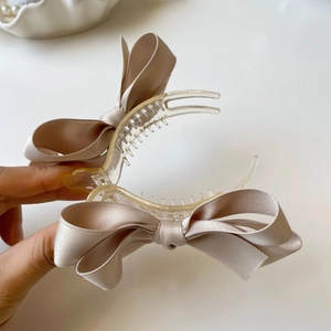 Dettaglio del fermaglio per capelli con fiocco in raso beige e impugnatura in plastica