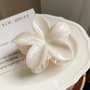 Close-up of a glossy cream white frangipani flower hair claw on a white ceramic plate