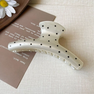 Close-up of cream French hair claw clip with black polka dots on a textured fabric