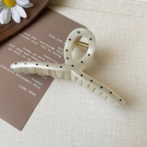 Detail view of cream-colored polka dot hair claw clip with strong gold metal spring