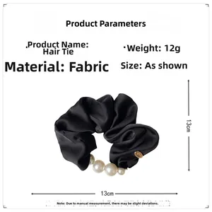 Detail view of a black satin scrunchie featuring large white pearls and a golden logo tag