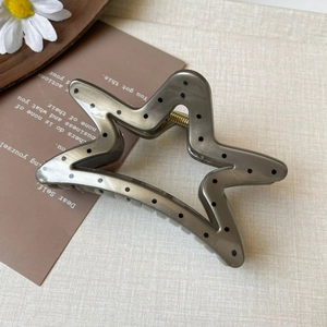 Detail view of a star-shaped hair claw clip with black polka dots on a grey surface