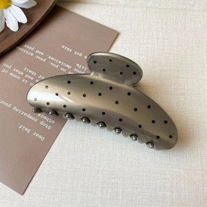Detailed close-up of a large grey polka dot shark clip hair claw on a woven background