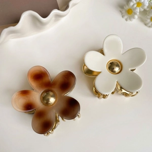 Détail de pinces à cheveux fleurs en acétate blanc crème et écaille sur un plateau