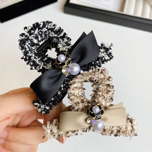 Close-up of elegant tweed hair claw with satin bow, faux pearl, and camellia detail