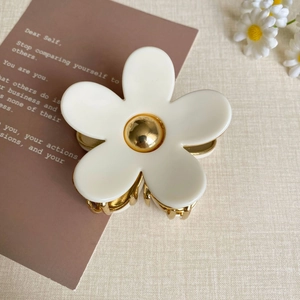 Gros plan sur la pince à cheveux fleur en acétate blanc avec pistil doré sur beige