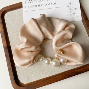 Detail of elegant champagne satin scrunchie with pearls and gold charm on display