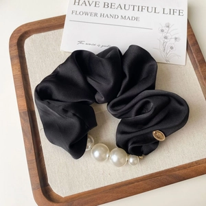 Detail view of a black silk scrunchie with gradient white pearls and a gold metal tag
