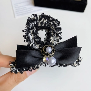 Detail of tweed hair claw clip featuring black satin bow, pearls and crystal embellishment