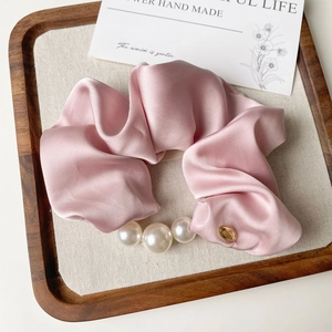 Detail of pink satin scrunchie featuring large white pearls and a gold metallic charm