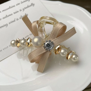 Pince à cheveux élégante avec nœud en soie champagne et perles sur une assiette en céramique