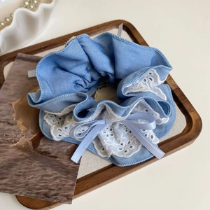 Macro shot of light blue denim scrunchie with white lace trim and bow detail