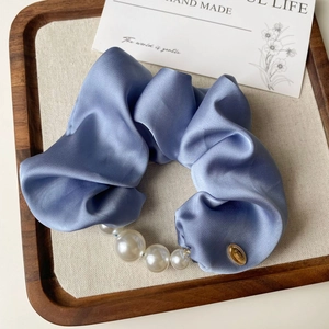 Detailed macro view of a light blue satin scrunchie with white faux pearls and gold pendant