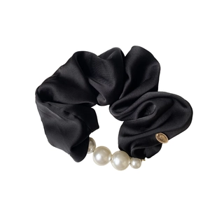 Elegant black satin hair scrunchie with gradient pearls and a gold logo charm on white background