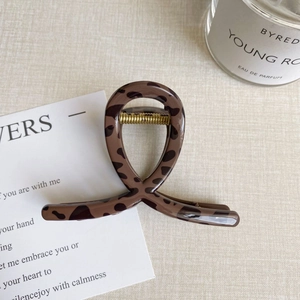 Detail of a large leopard print hair claw clip with a twisted design on a neutral desk