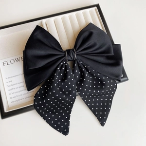 Detail of black satin bow hair clip with white polka dots and rhinestone center piece